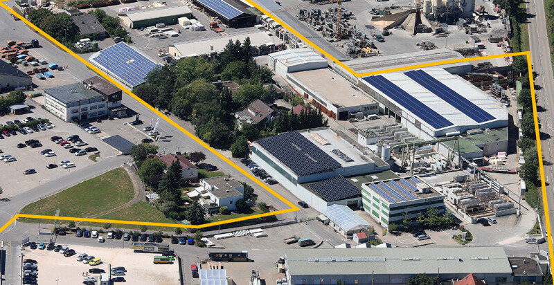 Luftbild eines Industriegeländes mit Solardächern, Firmengrundstück gelb markiert