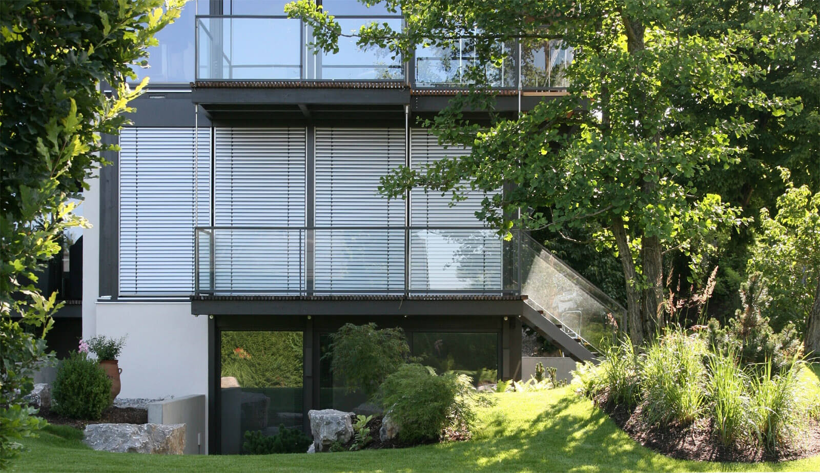Doppelvilla: Gartenfassade mit Jalousien, Glasbalkonen und Außentreppe hinter Ginkgo