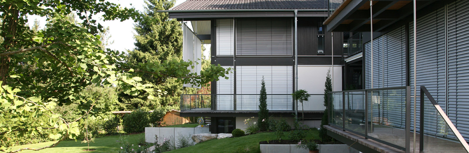 Doppelvilla: Gartenansicht mit Glasbalkonen, Jalousien und Ginkgobaum am Hang