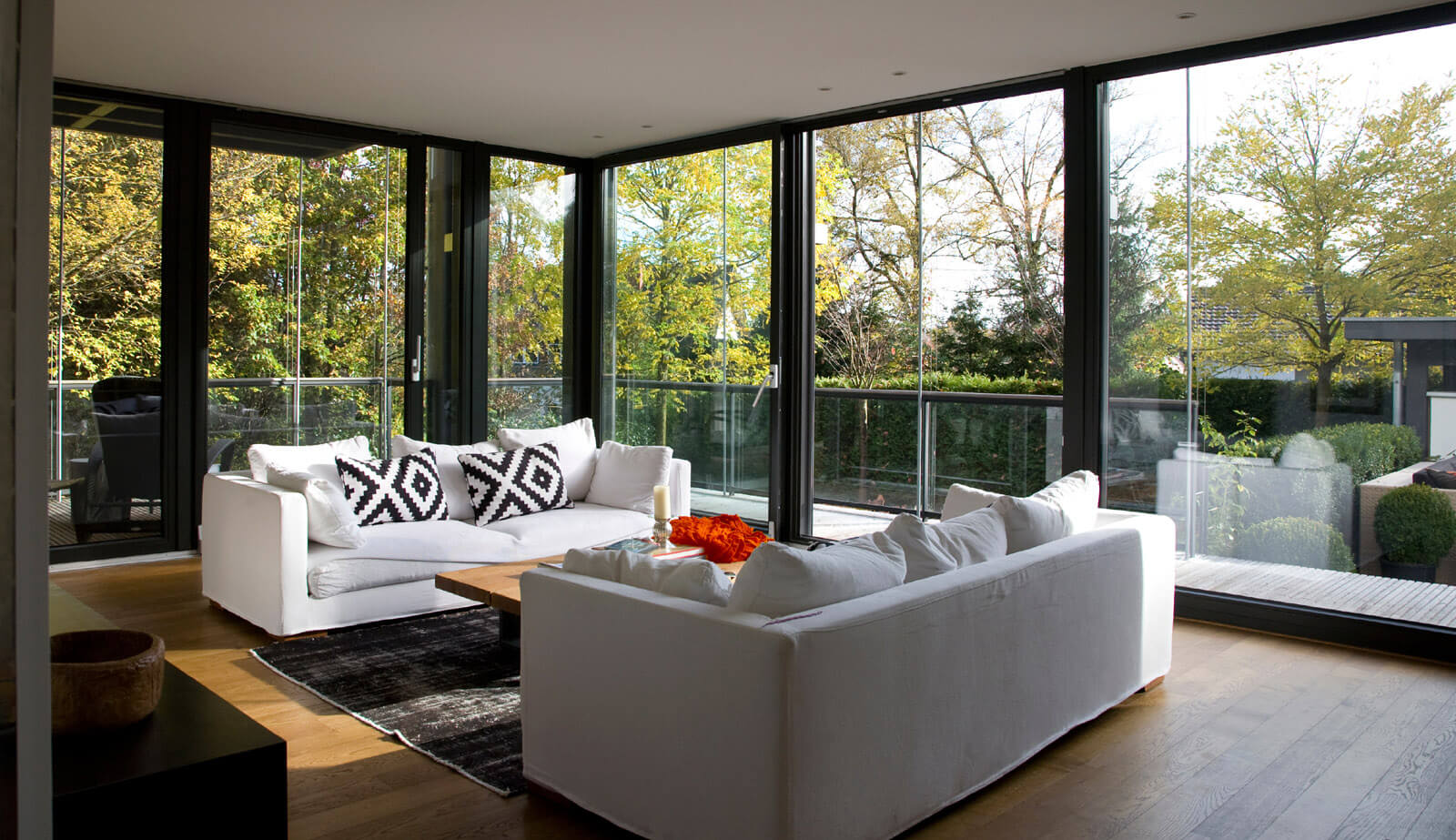 Flachdach-Kubus: Wohnraum mit weißen Sofas und Glaswänden zum Garten