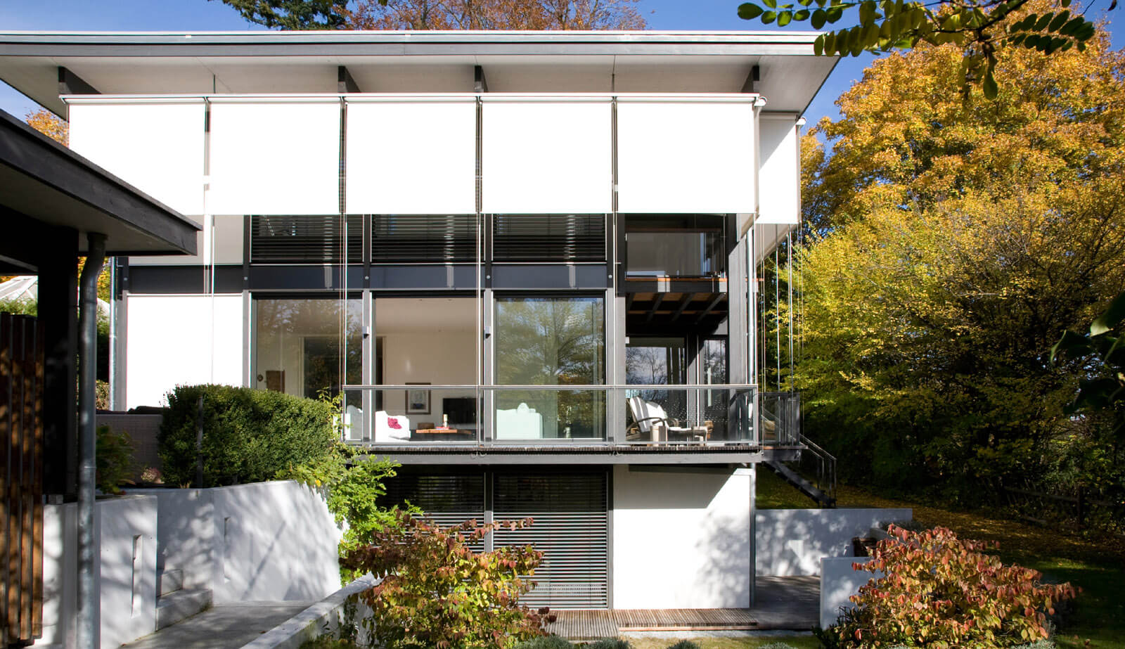 Flachdach-Kubus: Gartenansicht mit Sonnensegeln, Balkon und Herbstlaub