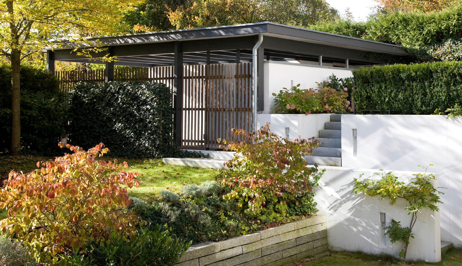 Flachdach-Kubus: Carport mit Holzlamellen und terrassierter Garten