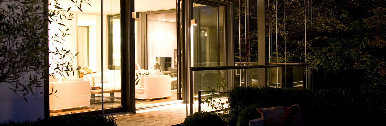 Flachdach-Kubus: erleuchteter Wohnraum hinter Glasschiebetüren bei Nacht