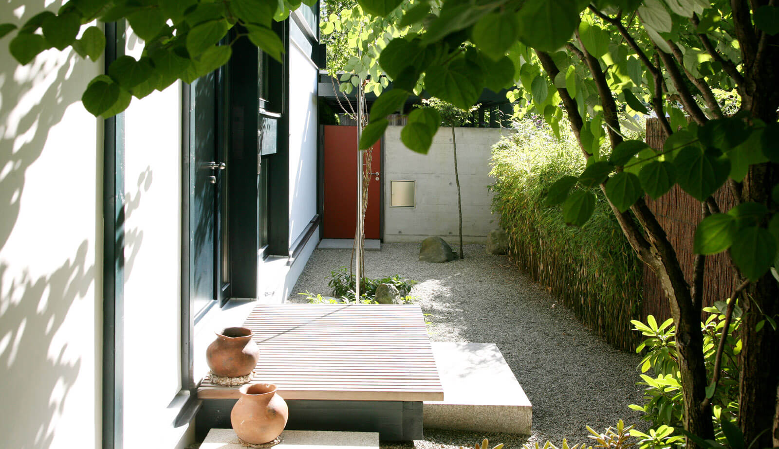 On a small plot: courtyard with timber bench, clay pots and gravel in the shade