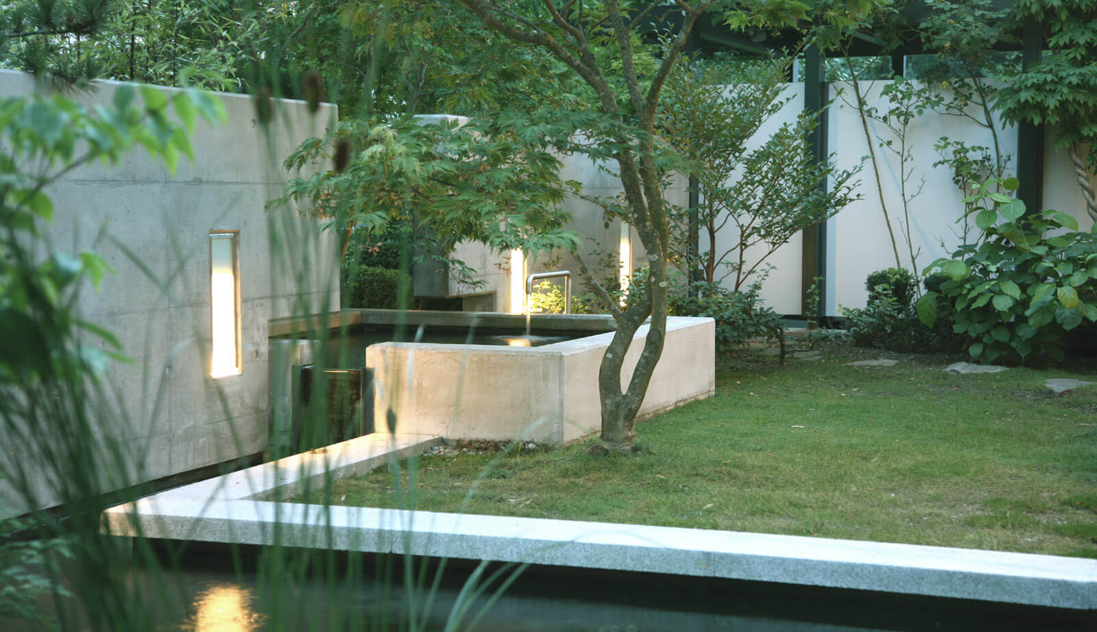On a small plot: lawn with concrete fountain basin and lit wall niches