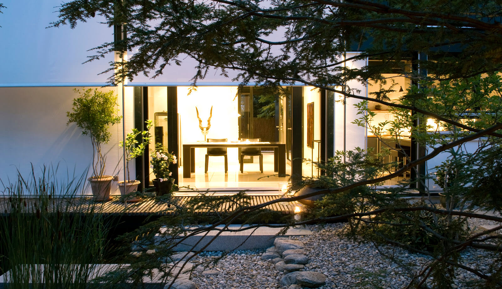 On a small plot: view across gravel garden to terrace and dining area at dusk