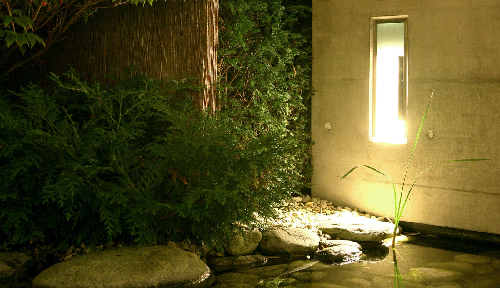On a small plot: lit wall niche in concrete wall above stones by the pond