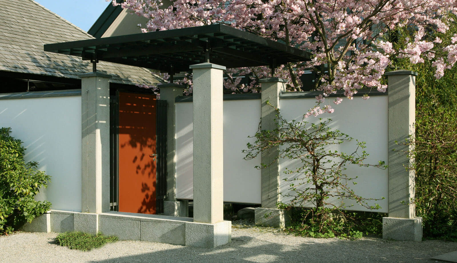 Haus am See: Eingangstor mit roter Tür, Pergola und Kirschblüte