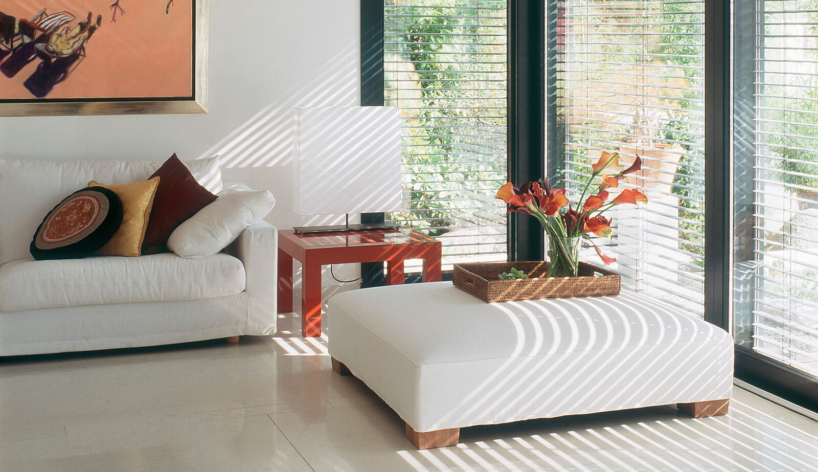 Haus am See: weißes Sofa und Hocker im Licht der Jalousien