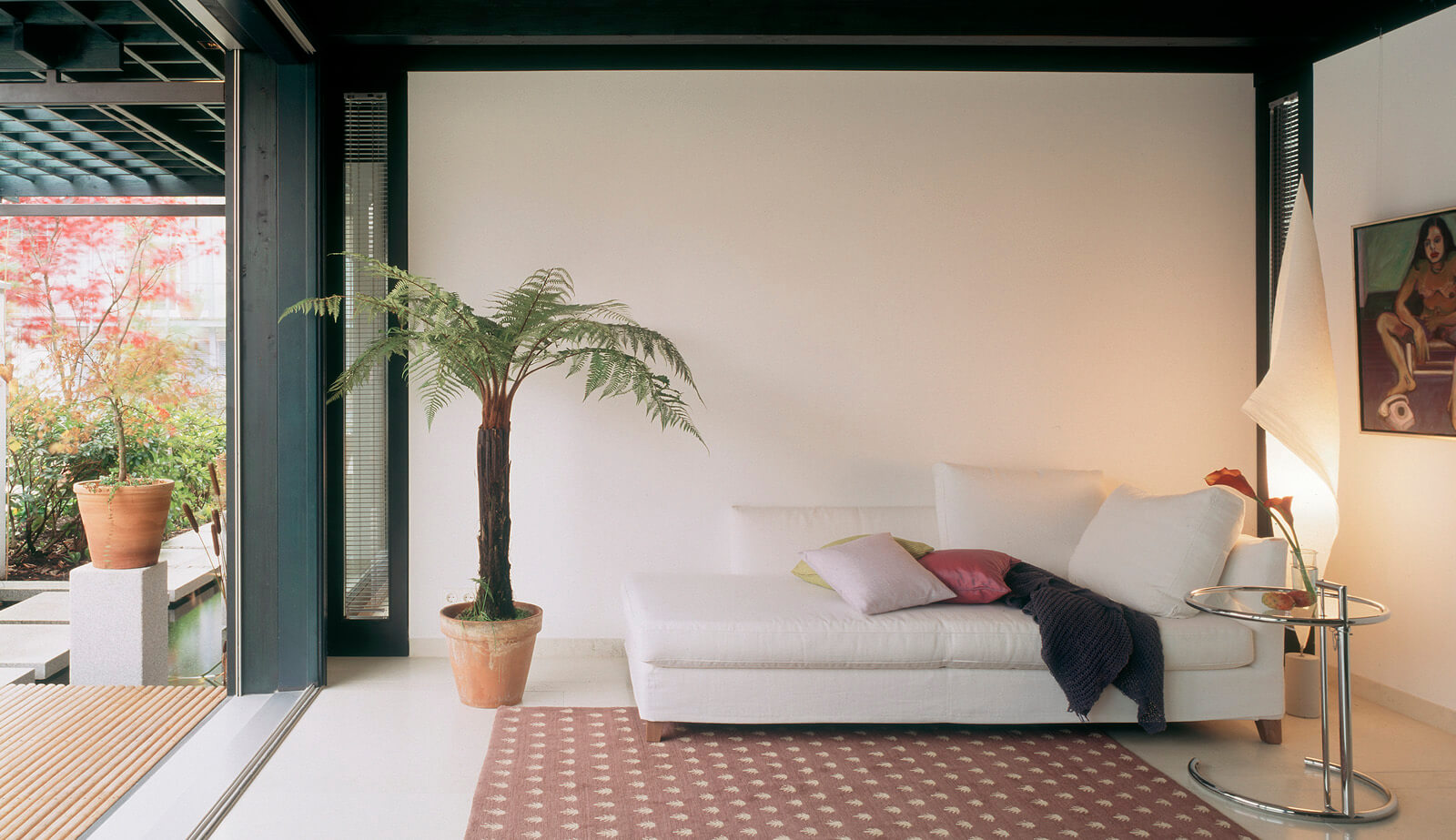 Haus am See: Wohnraum mit Sofa, Baumfarn und geöffneter Terrassentür