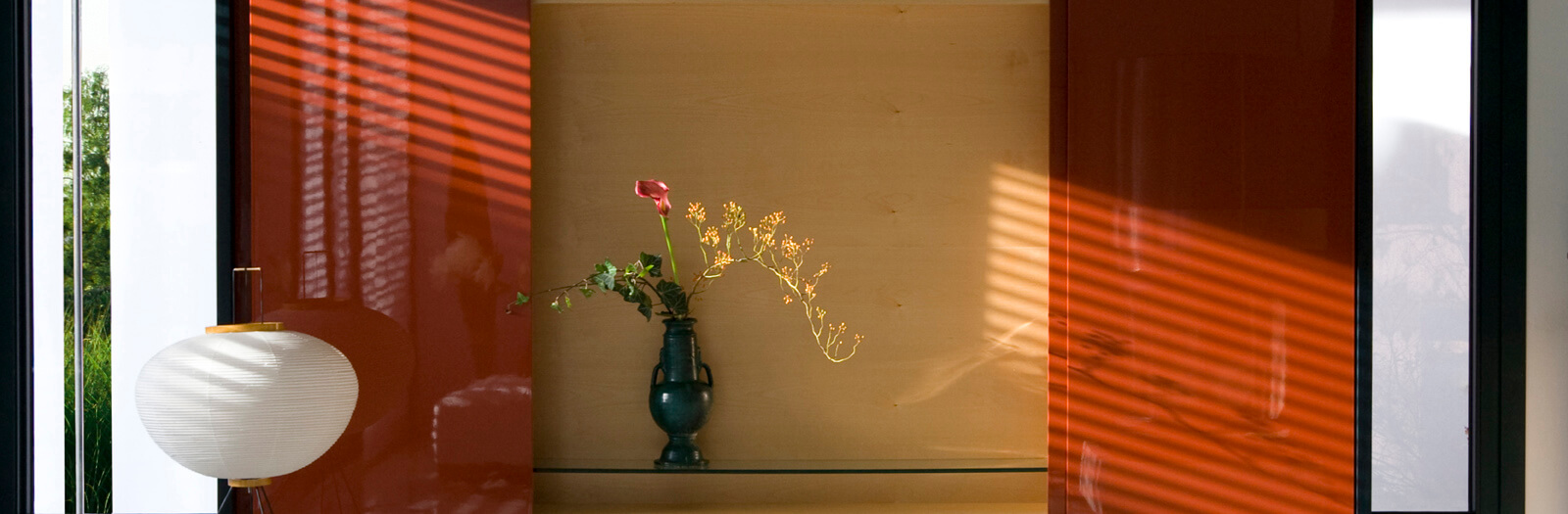 Haus am See: rote Lackvitrine mit Blumenvase und Papierleuchte
