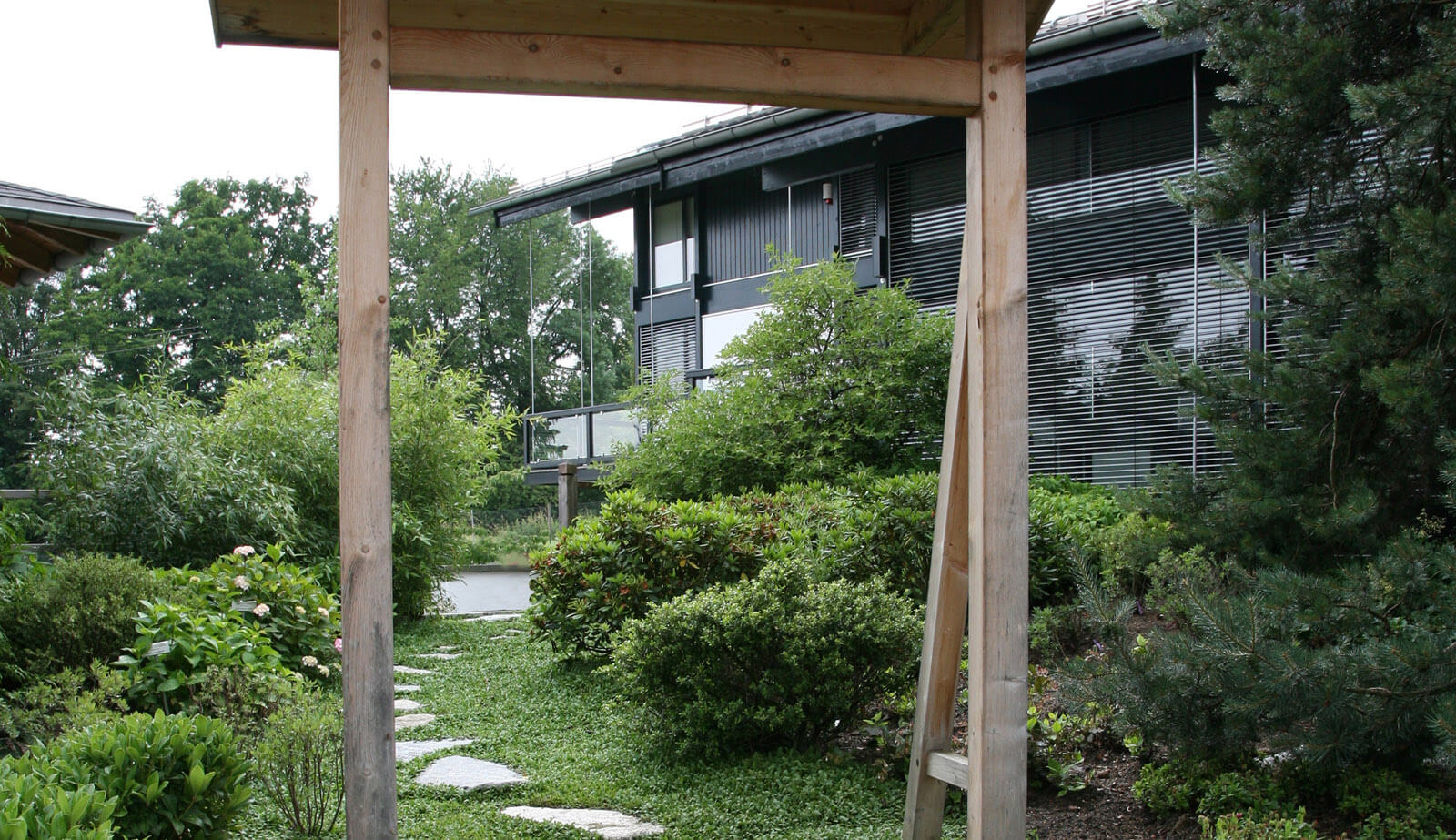 In der Baumschule: Blick durch das Holztor auf Garten und dunkle Holzfassade
