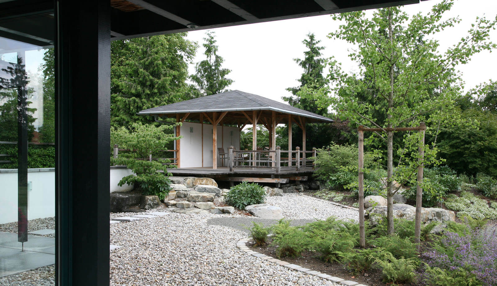 In der Baumschule: Blick unter dem Vordach auf Kiesgarten und Gartenpavillon