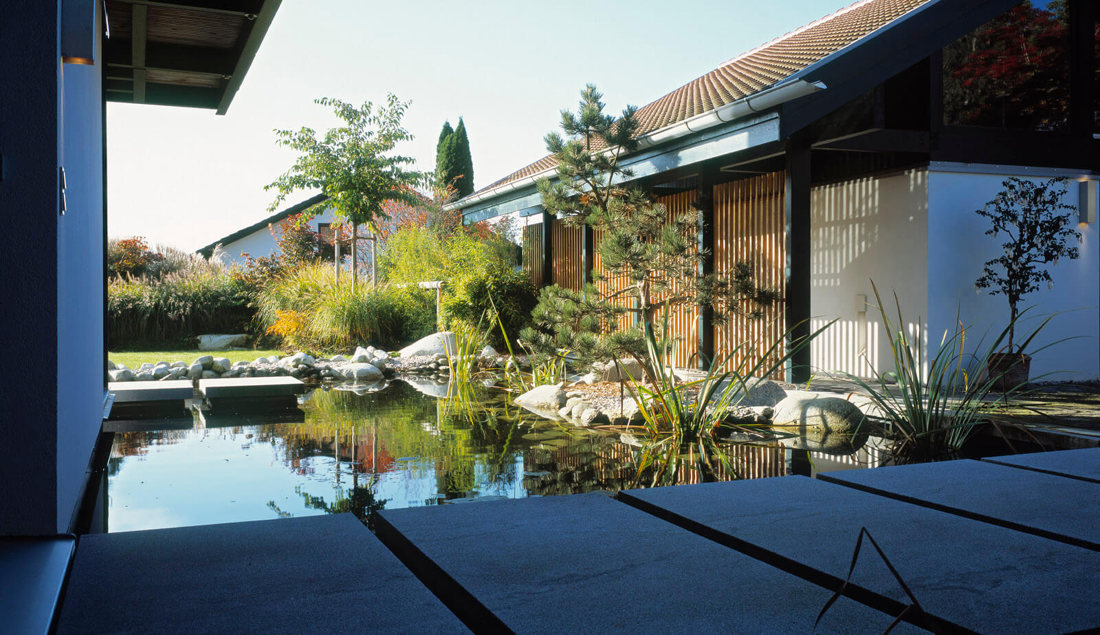 Haus in Hanglage: Teich mit Trittplatten vor der Holzfassade