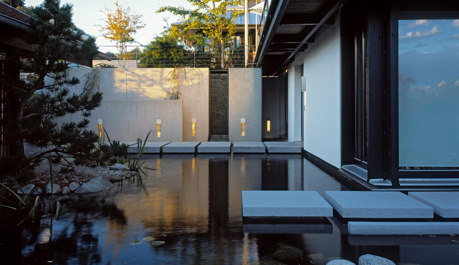 Haus in Hanglage: Teich mit Trittplatten und Wandleuchten am Abend