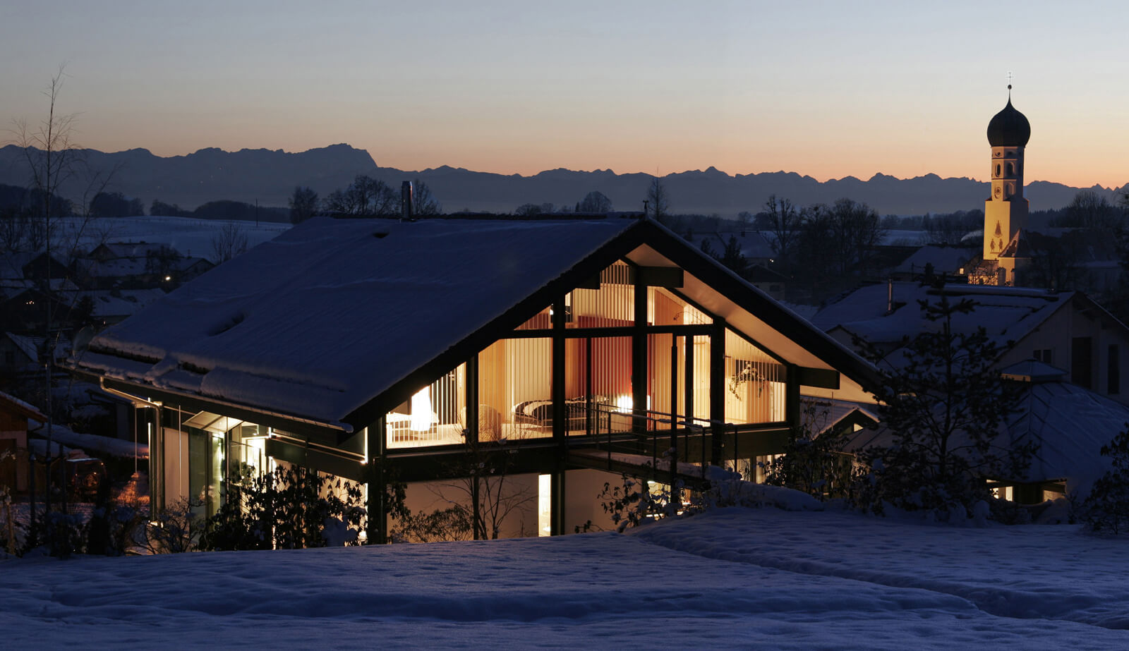 Haus in Hanglage im Schnee vor Alpenpanorama und Kirchturm