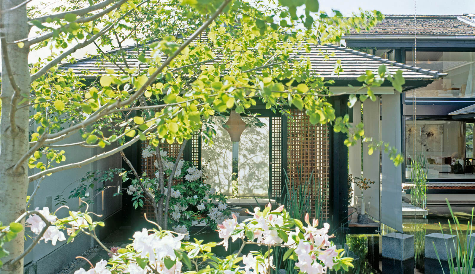 Haus mit Höfen: Gartenpavillon mit Holzgitter hinter blühenden Bäumen