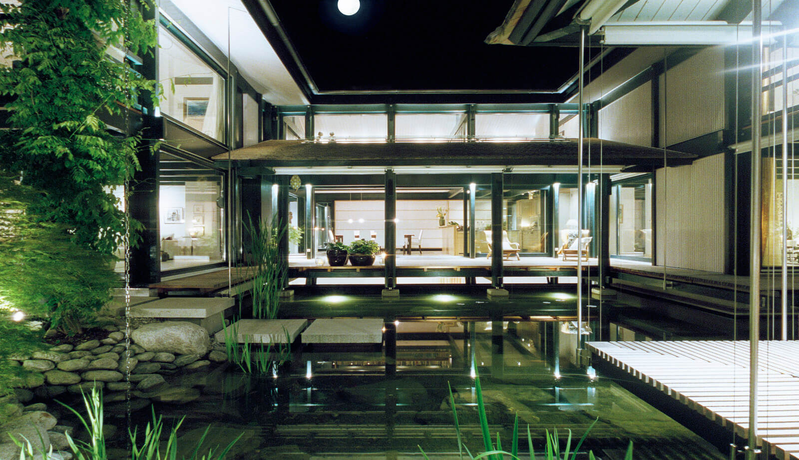Haus mit Höfen: Innenhof mit Koi-Teich und Holzsteg bei Nacht