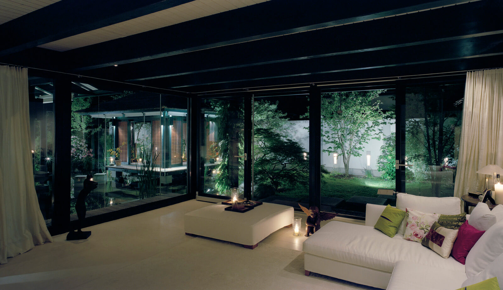 Haus mit Höfen: Wohnraum mit weißem Sofa und Blick in den nächtlichen Garten