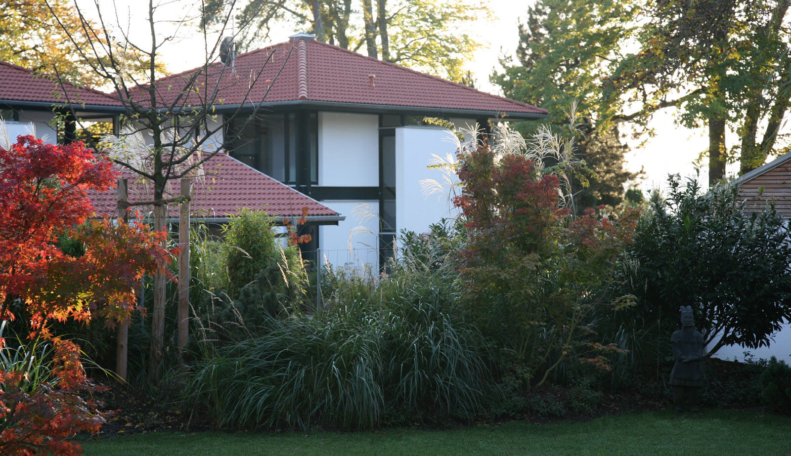 Stadthaus-Pärchen: Zeltdachhaus hinter Gräsern und rotem Ahorn im Herbst