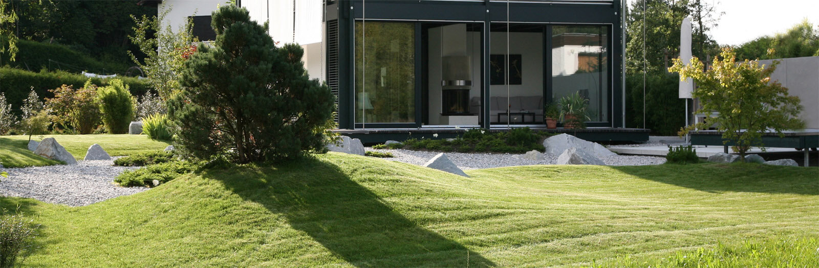 Am Biberteich: Glasfront des Wohnraums hinter gewelltem Rasen und Kiesflächen