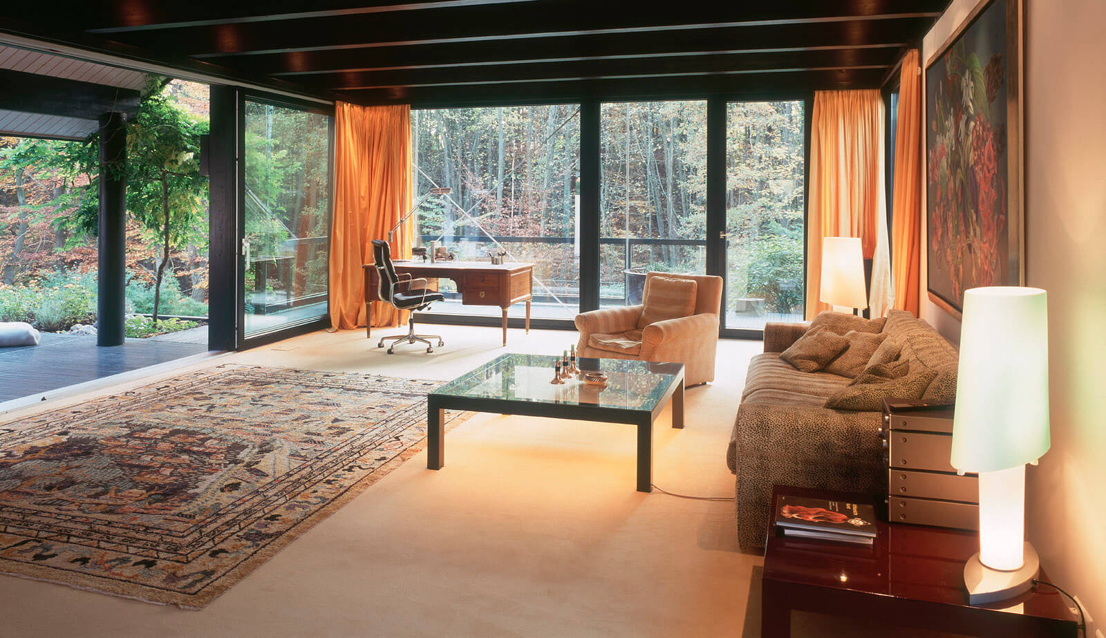 Villa im Park: Wohnraum mit Sofa, Glastisch und Fensterfront zum Wald
