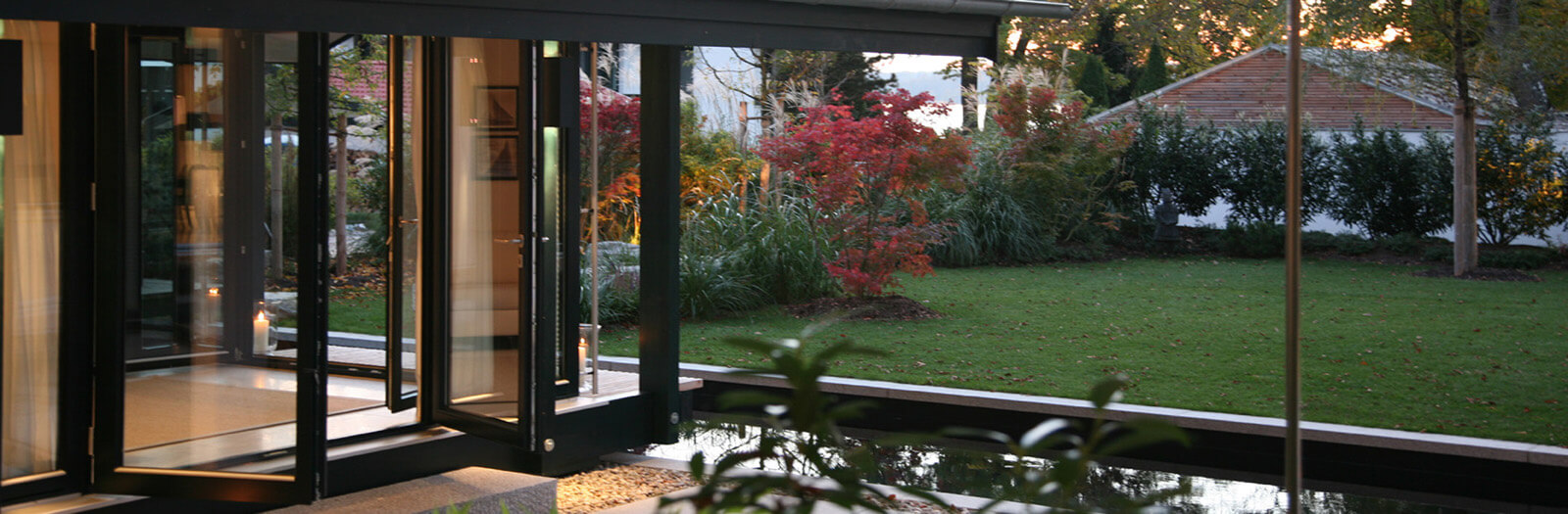 Haus mit Gästehaus: geöffnete Glasfront mit Blick auf Rasen und Herbstgarten