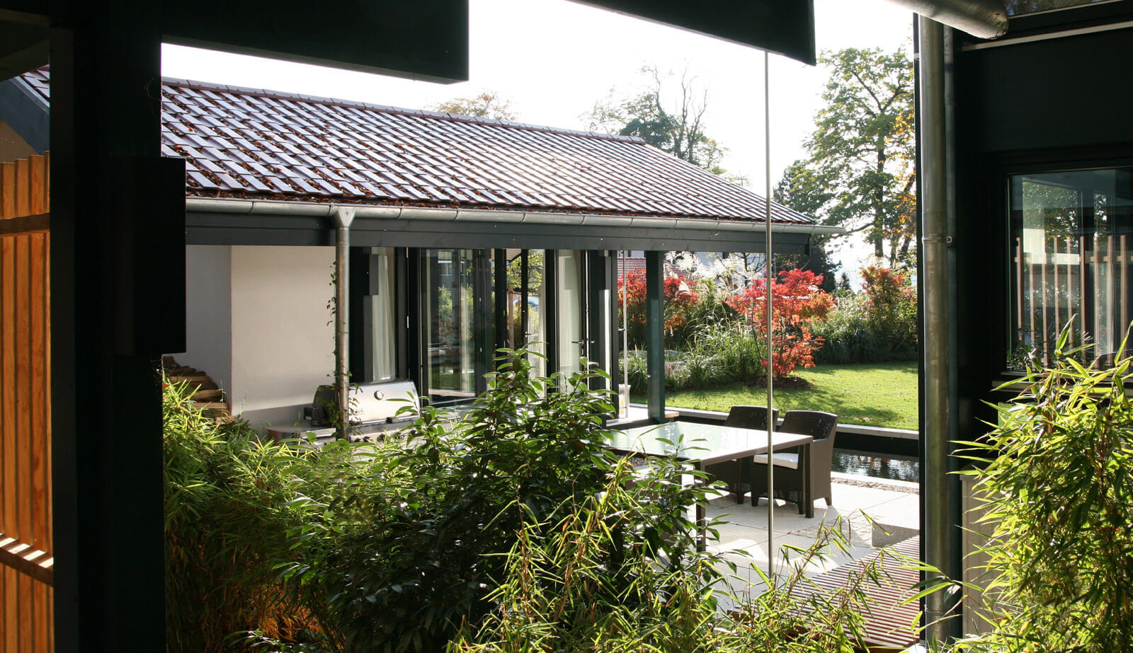 Haus mit Gästehaus: Blick durch Bambus auf überdachte Terrasse mit Sitzgruppe