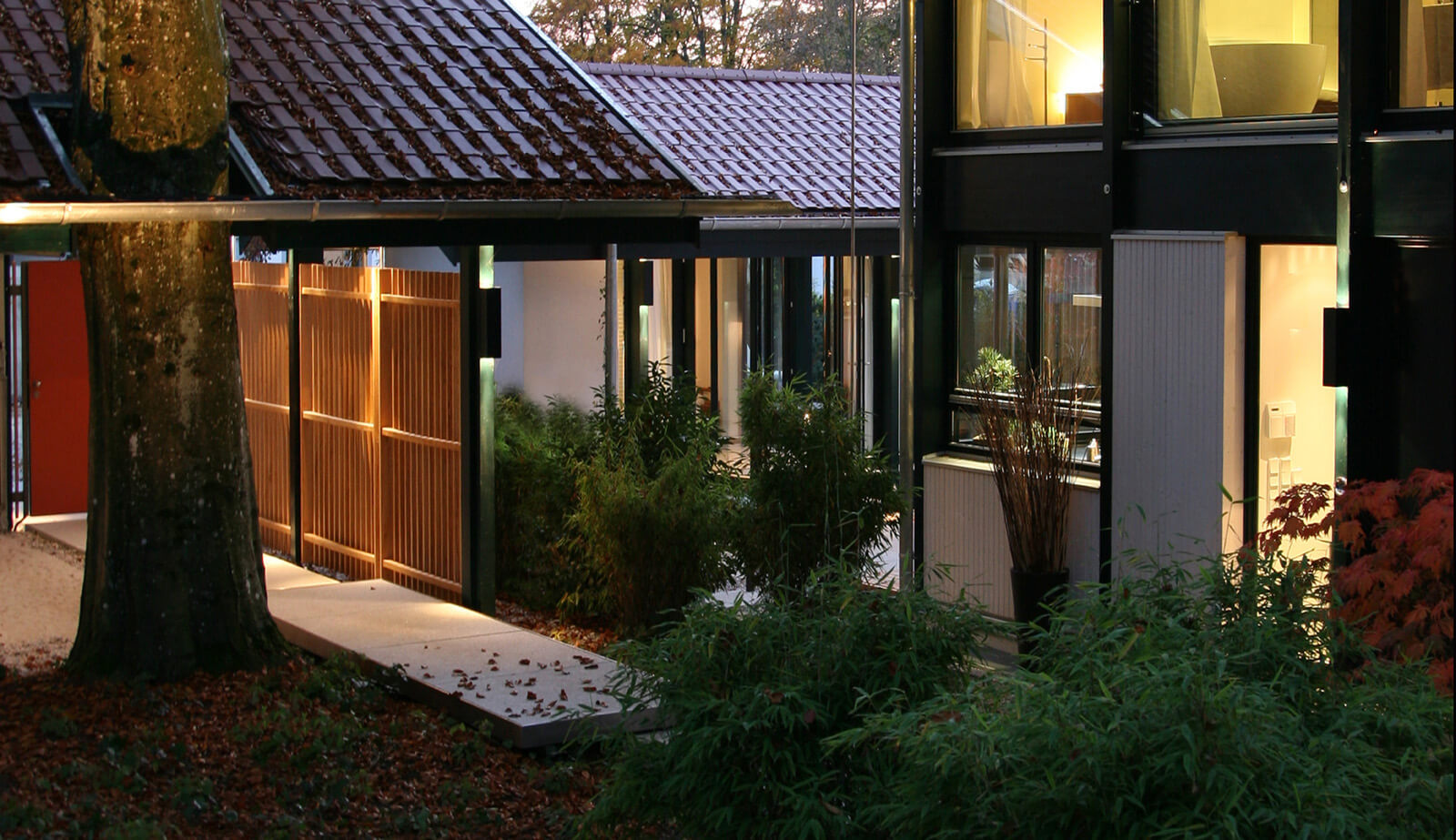 Haus mit Gästehaus: Eingangsweg mit Holzlattenzaun und beleuchteter Fassade