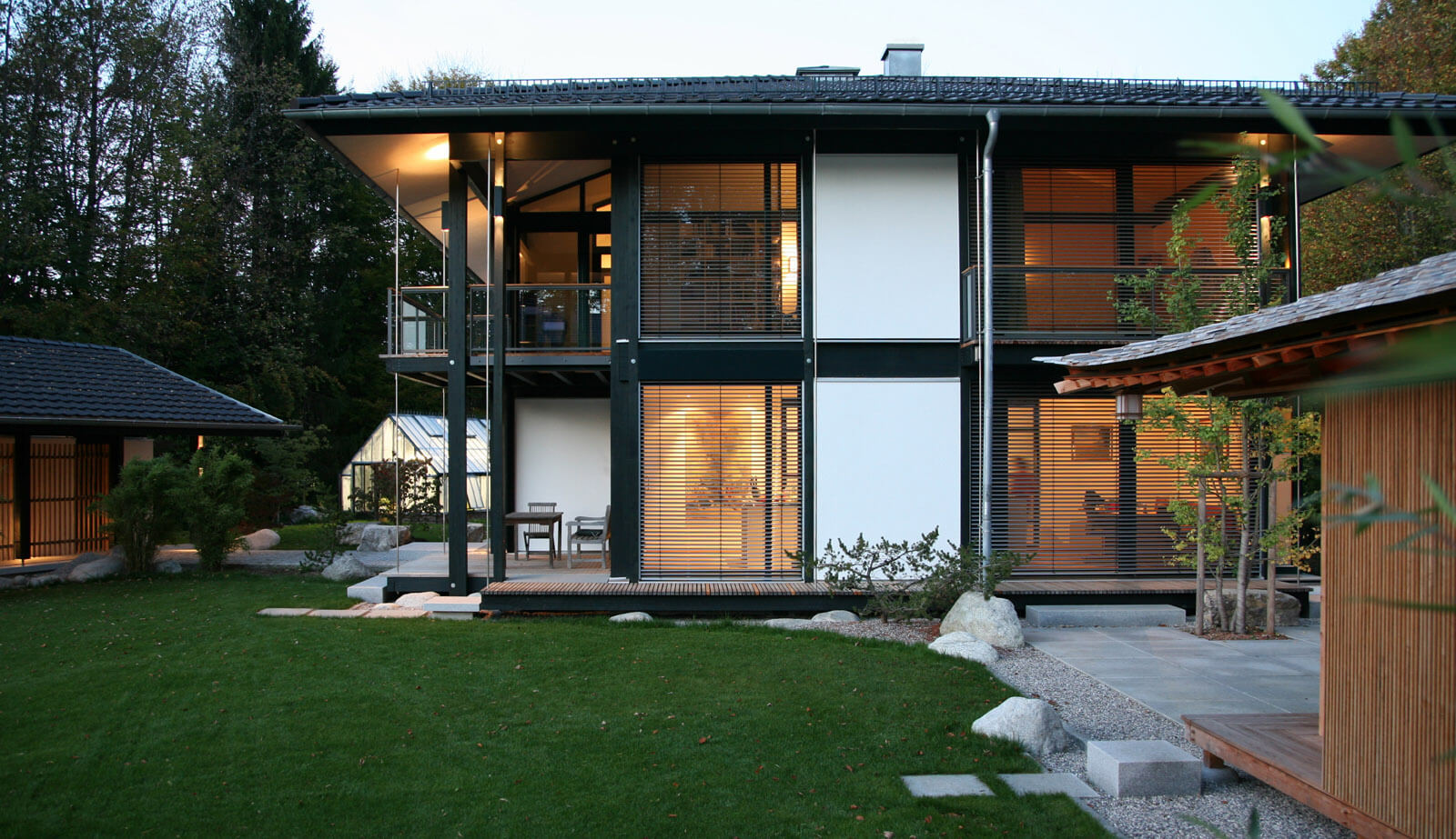 Zeltdachvilla: Gartenfassade mit Terrasse, Loggia und Gewächshaus am Abend