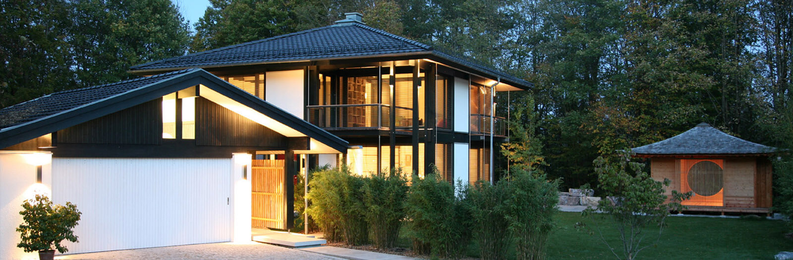 Zeltdachvilla: Haus mit Garage und Gartenhaus am Abend beleuchtet