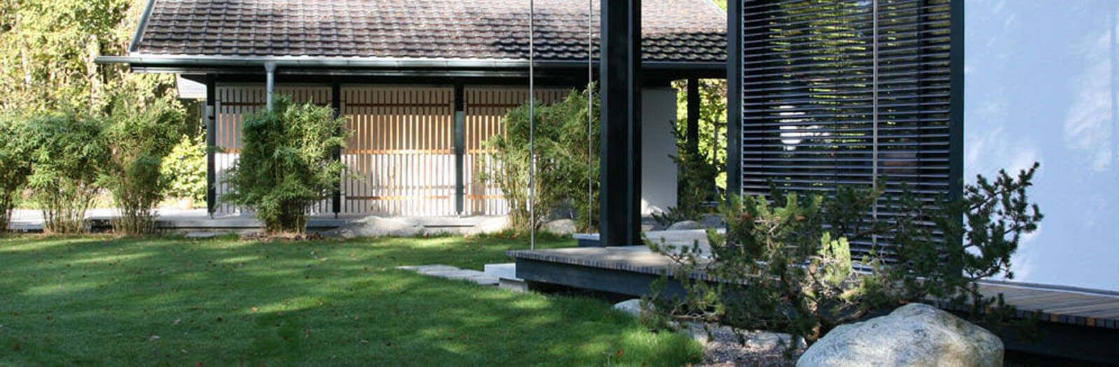 Zeltdachvilla: Garten mit Rasen, Findling und Nebengebäude mit Holzlamellen