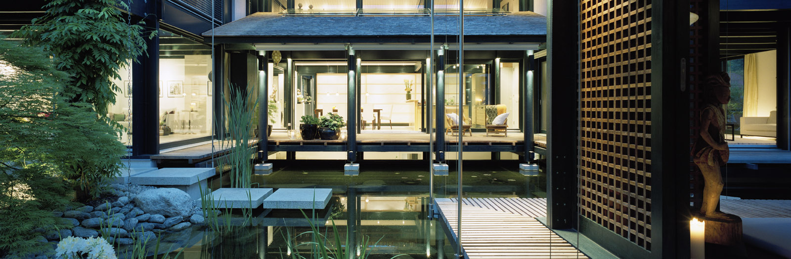 Haus mit Höfen: beleuchteter Innenhof mit Wasserbecken, Trittsteinen und Holzgitterwand am Abend