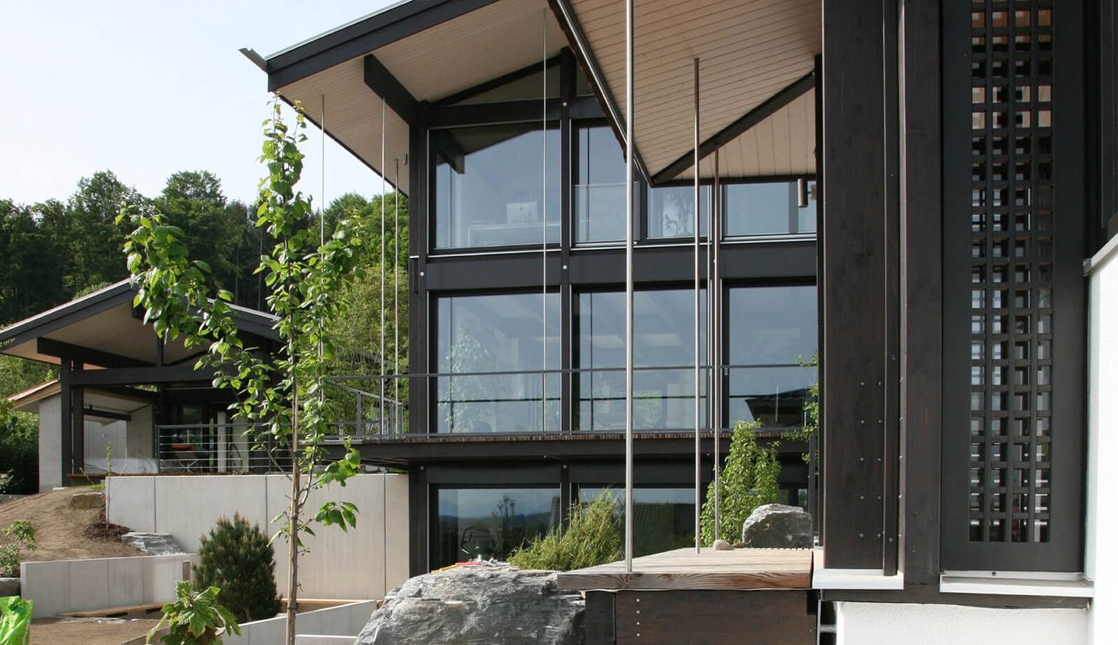 Villa mit Wellnesshaus: zweigeschossige Glasfassade mit Holzgitter und Findling
